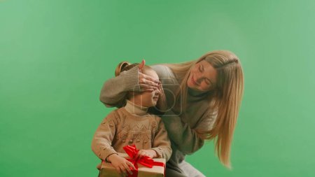Photo for Happy family sharing joy with each other on Christmas. Mom gives a surprise gift to her daughter and closes her eyes on green background - Royalty Free Image