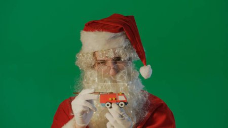 Foto de Retrato de Santa Claus pintando un coche con un regalo sobre un fondo verde - Imagen libre de derechos