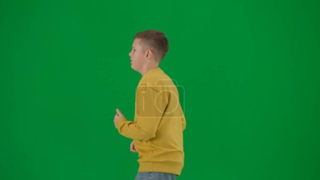 Photo for School kids and leisure time creative concept. Portrait of kid boy on chroma key green screen. Schoolboy in jeans running looking around. Middle body side shot. - Royalty Free Image