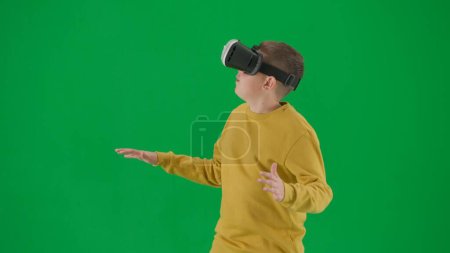 Photo for School kids and leisure time creative concept. Portrait of kid boy on chroma key green screen. Schoolboy in jeans wears virtual reality glasses amazed face expression. Middle body front shot. - Royalty Free Image