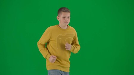 Photo for School kids and leisure time creative concept. Portrait of kid boy on chroma key green screen. Schoolboy in jeans running looking around. Middle body profile shot. - Royalty Free Image