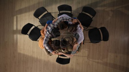 Photo for In the shot above a group of people, a man and a woman and their mentor are sitting on a chair. They have come to a meeting, a session, therapy. They are sitting in a circle hugging each other. - Royalty Free Image