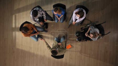 Photo for In the shot above, a group of people and their mentor are sitting on a chair. They have come to a meeting, a session, therapy. They are sitting in a circle chatting with their disabled person. - Royalty Free Image