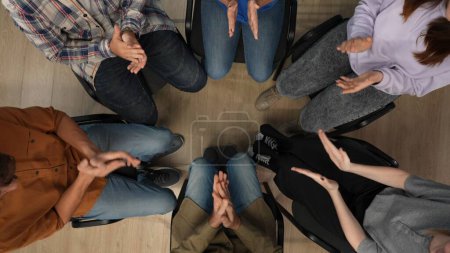Photo for In the shot above, man, a psychologist, a mentor, is sitting on a chair in the center. Across from him sits his group, they are having a meeting, therapy. They are applauding. Close up. - Royalty Free Image