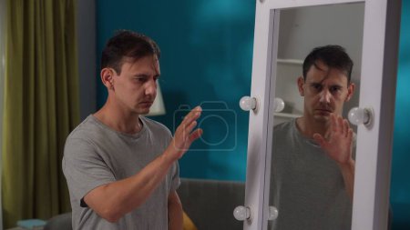 Téléchargez les photos : Un homme souffrant d'un trouble mental se tient devant un miroir, cachant son visage dans ses mains tout près. Apathie, conflit intérieur, problèmes psychologiques - en image libre de droit