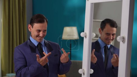 Téléchargez les photos : Un homme en costume strict est debout dans le salon devant un miroir de près. Personnalité partagée - en image libre de droit