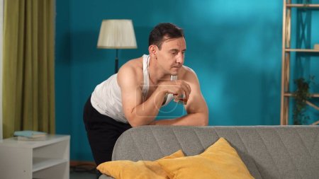 Foto de Un hombre con un vaso de alcohol se apoya en un sofá en la sala de estar. Trastorno bipolar, personalidades divididas - Imagen libre de derechos