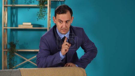 Photo for A man in a business suit stands leaning against the back of a sofa in the living room close up. Split personality, hallucinations, smartphone addiction - Royalty Free Image