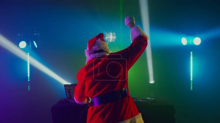 Téléchargez les photos : DJ Santa Claus mixant des morceaux dans une boîte de nuit lors d'une fête de Noël et du Nouvel An ou d'événements d'entreprise. Senior disc jockey comme Santa écouter de la musique, écouteurs, ordinateur portable, lecteur de contrôleur de mélangeur, platine - en image libre de droit