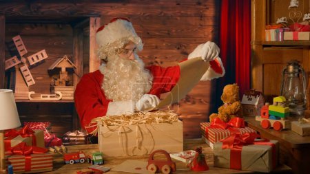 Photo for Santa Claus at the table with gifts and reading a letter at his house - Royalty Free Image