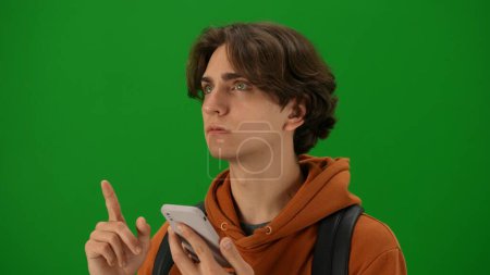 Photo for Airport creative advertisement concept. Portrait of person tourist isolated on chroma key green screen background. Close up shot young man holding smartphone looking at the departure board. - Royalty Free Image