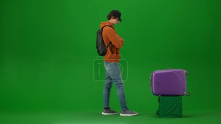 Téléchargez les photos : Concept publicitaire créatif aéroport. Portrait de touriste de personne isolé sur fond d'écran vert clé chroma. Jeune homme debout attendant sa valise au carrousel à bagages. - en image libre de droit