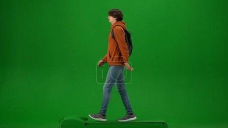 Foto de Concepto de publicidad creativa del aeropuerto. Retrato de persona turística aislado en croma pantalla verde clave de fondo. Hombre joven con capucha naranja con mochila caminando y mirando a su alrededor. - Imagen libre de derechos
