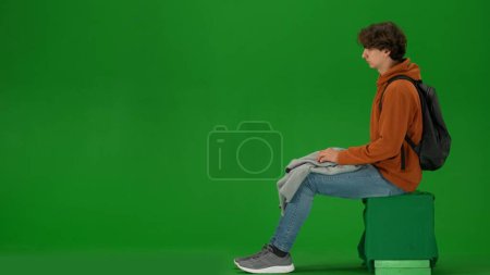 Foto de Concepto de publicidad creativa del aeropuerto. Retrato de persona turística aislado en croma pantalla verde clave de fondo. Joven sentado sosteniendo a cuadros listo para tomar la siesta esperando el vuelo. - Imagen libre de derechos