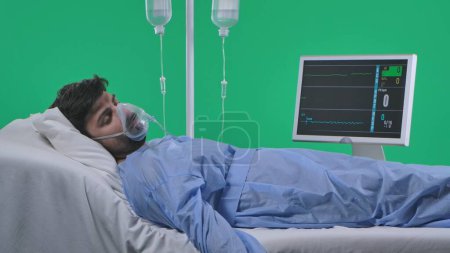 Photo for Medical ward and rehabilitation creative concept on chroma key green screen. Adult man patient laying in bed with drip, breathing mask and monitor, lost consciousness, coma heart rate stopped. - Royalty Free Image