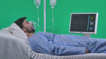 Photo for Medical ward and rehabilitation creative concept on chroma key green screen. Adult man patient laying in bed with drip, breathing mask and monitor, shocked face expression looking around. - Royalty Free Image