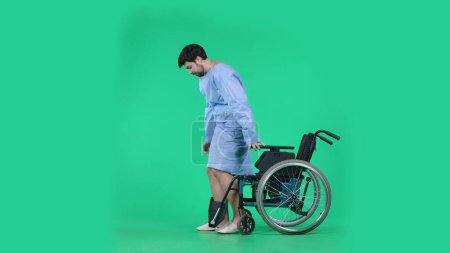 Photo for Medical ward and rehabilitation creative concept on chroma key green screen. Adult man patient in robe standing from wheelchair ready to make few steps without support, focused expression. - Royalty Free Image