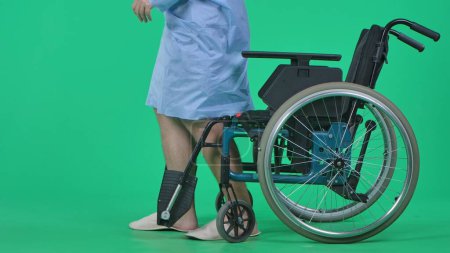 Photo for Medical ward and rehabilitation creative concept on chroma key green screen. Adult man patient in robe standing from wheelchair and making few steps without support, close up shot. - Royalty Free Image