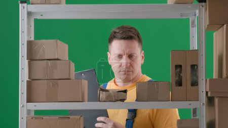 Photo for In the frame on a green background, chromakey. Depicts an adult man in a working uniform. Demonstrates the storekeeper in a warehouse. He is got a tablet in his hand, and he is staring at the box. - Royalty Free Image