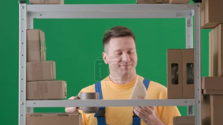 Photo for Framed on green background, chromakey. Depicted is an adult male wearing a work uniform. Demonstrates a storekeeper in a warehouse. He is holding a cup with a drink and smiling, he is happy, satisfied - Royalty Free Image