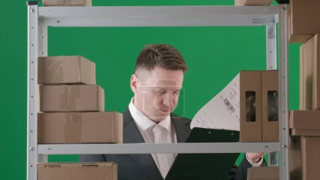 Photo for Framed on a green background, chromakey. Depicts an adult male in a suit. Demonstrates a manager, a supervisor in a warehouse. He skeptically, carefully looking through, studying documents on a tablet - Royalty Free Image