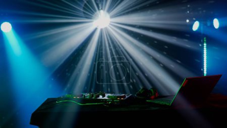 Foto de Esta cautivadora imagen muestra una configuración de DJ en medio de un vibrante espectáculo de luz, con haces de luz verde y azul creando un efecto dramático sobre la mesa de DJ. La neblina del ambiente del club - Imagen libre de derechos