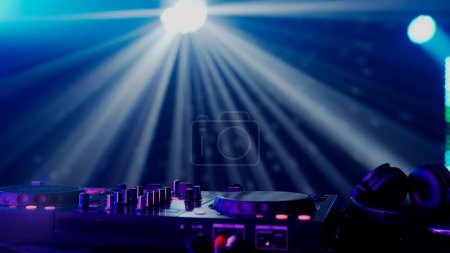 Foto de Esta cautivadora imagen muestra una configuración de DJ en medio de un vibrante espectáculo de luz, con haces de luz verde y azul creando un efecto dramático sobre la mesa de DJ. La neblina del ambiente del club - Imagen libre de derechos