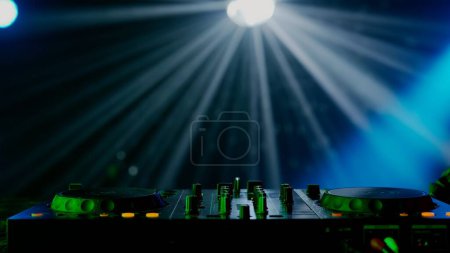 Téléchargez les photos : Cette image captivante présente une installation DJ au milieu d'un spectacle lumineux vibrant, avec des faisceaux de lumière verte et bleue créant un effet dramatique au-dessus de la table DJ. La brume de l'atmosphère du club - en image libre de droit