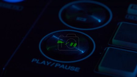 Téléchargez les photos : L'image capture un gros plan d'un bouton pause de lecture de consoles DJ, éclairé par une subtile lumière au néon qui donne vie à la surface de contrôle. C'est un détail qui montre les outils de précision à la - en image libre de droit
