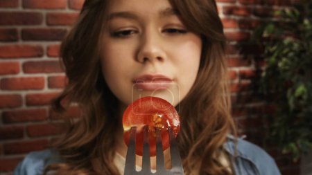 Foto de Primer plano de una chica mirando un tenedor con la mitad de un tomate rojo cereza maduro. Concepto creativo de publicidad de alimentos. POV - Imagen libre de derechos