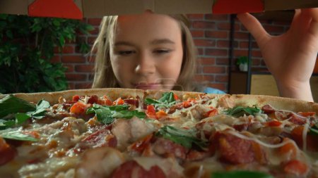 Téléchargez les photos : Vue de la boîte à pizza. Une fille ouvre une boîte à pizza avec une expression heureuse sur son visage. Concept créatif pour une publicité alimentaire. Point de vue. Gros plan - en image libre de droit