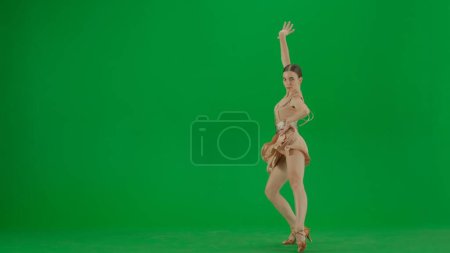 Téléchargez les photos : Latin Ballroom Dancer in Pose Against Green Screen. Une danseuse de salle de bal latine se dresse sur un fond d'écran vert, sa forme exsudant élégance et contrôle. Vêtue d'une robe de danse beige avec - en image libre de droit