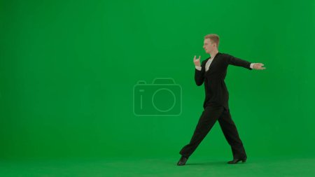 Photo for Ballroom Dancer Poised for Performance on Green Screen. A confident ballroom dancer stands poised in a classic dance stance, ready to begin his routine. Dressed in professional dance attire against a - Royalty Free Image