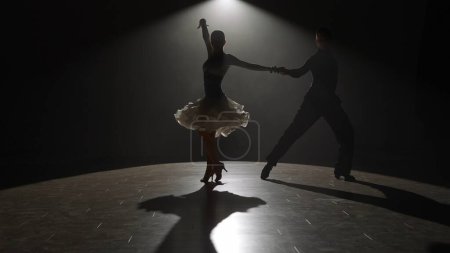 Photo for Elegant Ballroom Dance Couple on Spotlight. This striking image captures a ballroom dancing couple mid-performance, enveloped in a singular spotlight against the darkness, highlighting their form and - Royalty Free Image