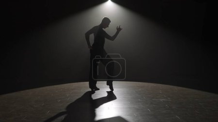 Téléchargez les photos : Silhouette Élégante danseuse de salon à l'honneur. La silhouette saisissante d'un danseur masculin est capturée sous un seul projecteur sur une scène sombre, transmettant un moment d'intensité dramatique. La lumière - en image libre de droit