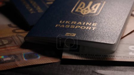 Téléchargez les photos : Passeport et migration concept publicitaire créatif. Gros plan d'une pièce d'identité humaine et du papier-monnaie. Billets en euros et passeport ukrainien sont disposés sur la table - en image libre de droit