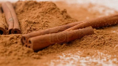 Photo for Aromatic spices creative concept advertisement. Close-up studio shot of spices. Brown aromatic cinnamon sticks lying on a pile of ground cinnamon powder. A shot for a coffee shop or restaurant - Royalty Free Image