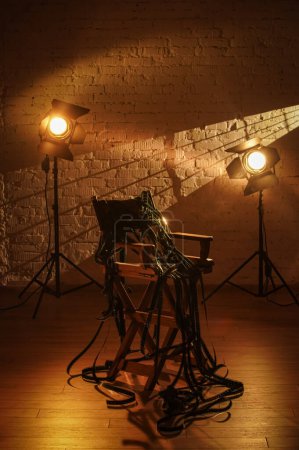Photo for Movie set and backstage creative advertisement concept. Close up shot of cinema set, clapperboard standing on directors chair, projectors at the background, many long film reel laying on the chair. - Royalty Free Image