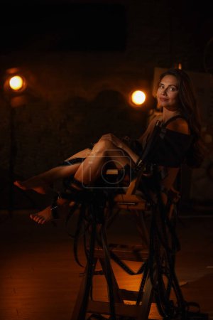 Photo for Movie set and backstage creative advertisement concept. Portrait of Beautiful woman actress. Brunette model with makeup in lingerie sitting on directors chair tangled in film reels, smiling expression - Royalty Free Image