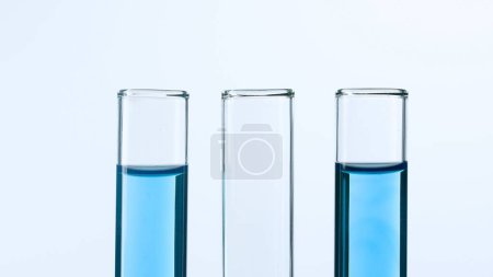 Foto de Tres tubos de ensayo de vidrio sobre fondo blanco. Dos tubos de ensayo están llenos de líquido azul y uno está vacío. Concepto de medicina, investigación bioquímica. Primer plano - Imagen libre de derechos