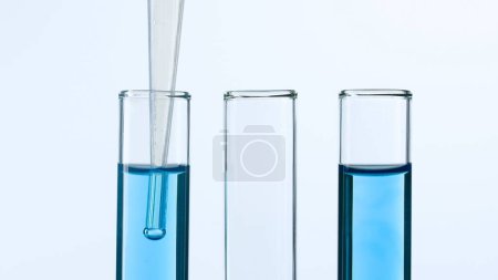 Téléchargez les photos : Trois éprouvettes en verre sur fond blanc. Deux éprouvettes sont remplies de liquide bleu et une pipette est descendue dans l'une d'elles. Concept de médecine, recherche biochimique. Gros plan - en image libre de droit