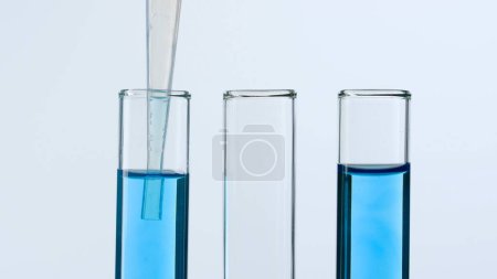 Foto de Tres tubos de ensayo de vidrio sobre fondo blanco. Dos tubos de ensayo están llenos de líquido azul y una pipeta se baja en uno de ellos. Concepto de medicina, investigación bioquímica. Primer plano - Imagen libre de derechos