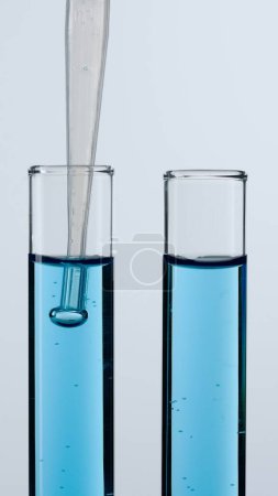 Foto de Dos tubos de vidrio sobre un fondo blanco. Los tubos de ensayo están llenos de líquido azul, una pipeta se baja en uno de ellos. Concepto de medicina, investigación bioquímica. Primer plano. - Imagen libre de derechos