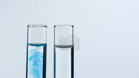 Foto de Dos tubos de ensayo de vidrio sobre fondo blanco. Los tubos de ensayo están llenos de líquido transparente, uno muestra una sustancia azul disolvente. Concepto de medicina, investigación bioquímica. Primer plano - Imagen libre de derechos
