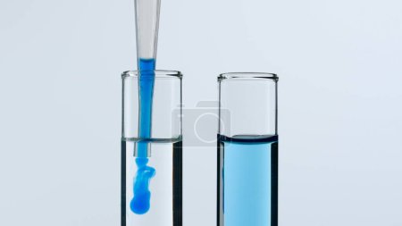Foto de Dos tubos de ensayo de vidrio sobre fondo blanco. Los tubos de ensayo están llenos de líquido, una sustancia azul gotea en uno de ellos desde una pipeta. Concepto de medicina, investigación bioquímica. Primer plano - Imagen libre de derechos