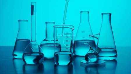 Photo for Science and biotechnology creative concept. Close up medical glassware on neon background. Laboratory table with many different beakers and test tubes with liquid for experiments in blue neon light. - Royalty Free Image