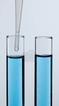 Foto de Dos tubos de vidrio sobre un fondo blanco. Los tubos de ensayo están llenos de líquido azul, una pipeta se baja en uno de ellos. Concepto de medicina, investigación bioquímica. De cerca.. - Imagen libre de derechos