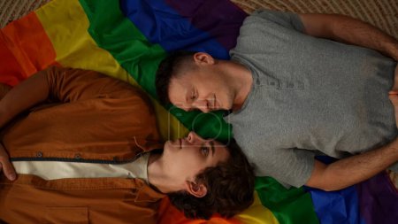 Téléchargez les photos : Prise de vue de dessus d'un couple homosexuel, bisexuel, pansexuel et transgenre posé sur le drapeau LGBT, se regardant, encourageant l'amour, l'égalité, la liberté. Contenu éducatif, liberté d'amour, fierté. - en image libre de droit