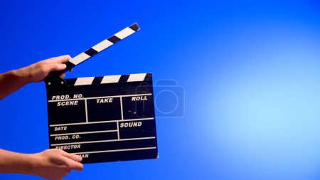 Photo for Hand is holding Black clapper board or movie slate on a blue background with a circular light. Cinema industry, entertainment - Royalty Free Image