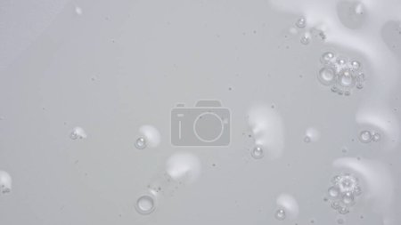 Foto de Concepto de publicidad creativa en gel y líquido. Primer plano de sustancia transparente sobre el fondo blanco. Gel de producto cosmético o suero con burbujas que fluyen en la superficie. - Imagen libre de derechos